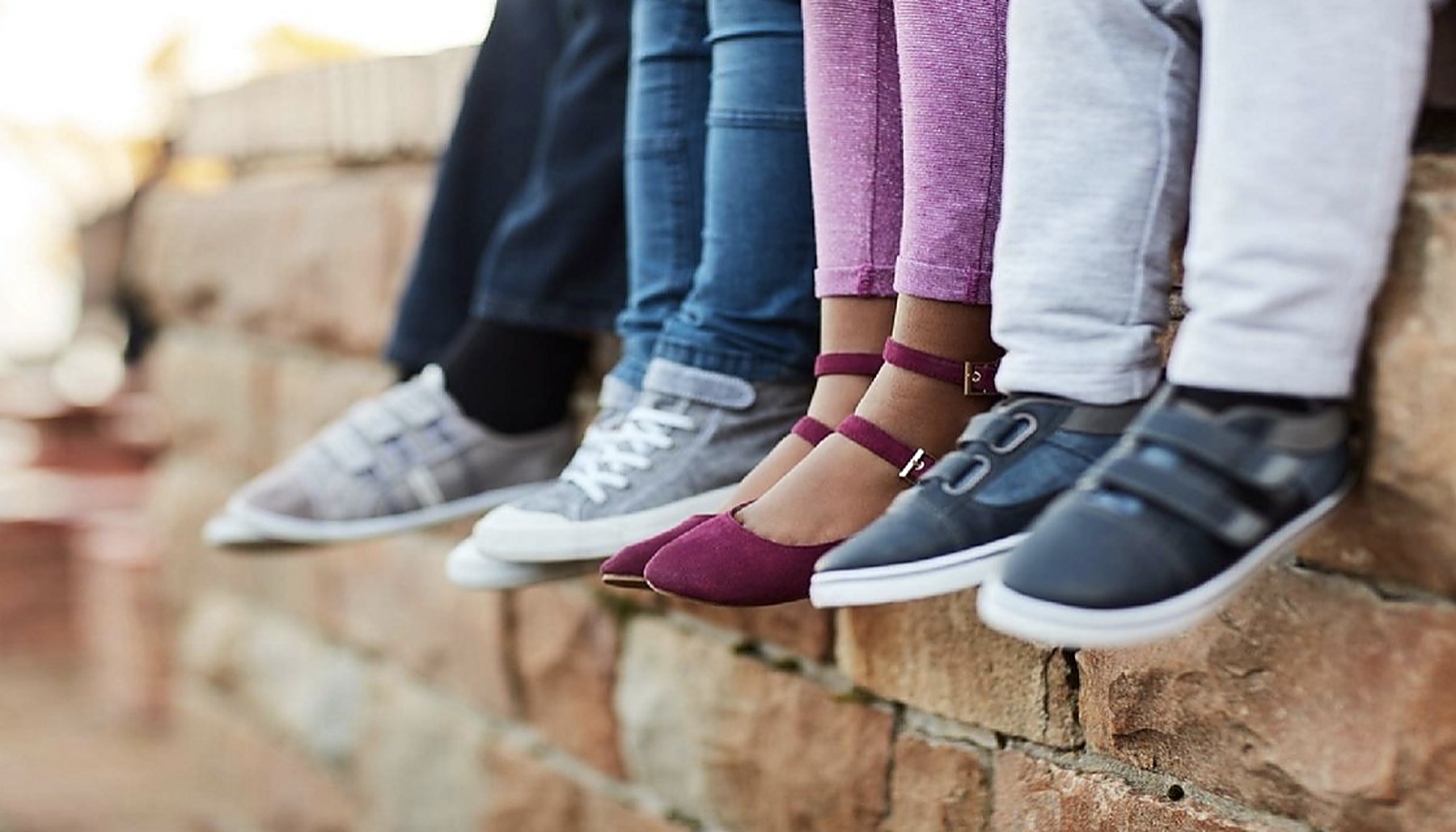 Children's feet in colorful brand-new shoes, sitting on a wall